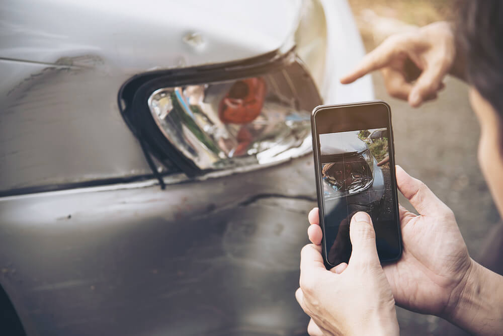 Hombre sacando una foto con el móvil a un coche averiado durante el atestado Hombre sacando una foto con el móvil a un coche averiado durante el atestado