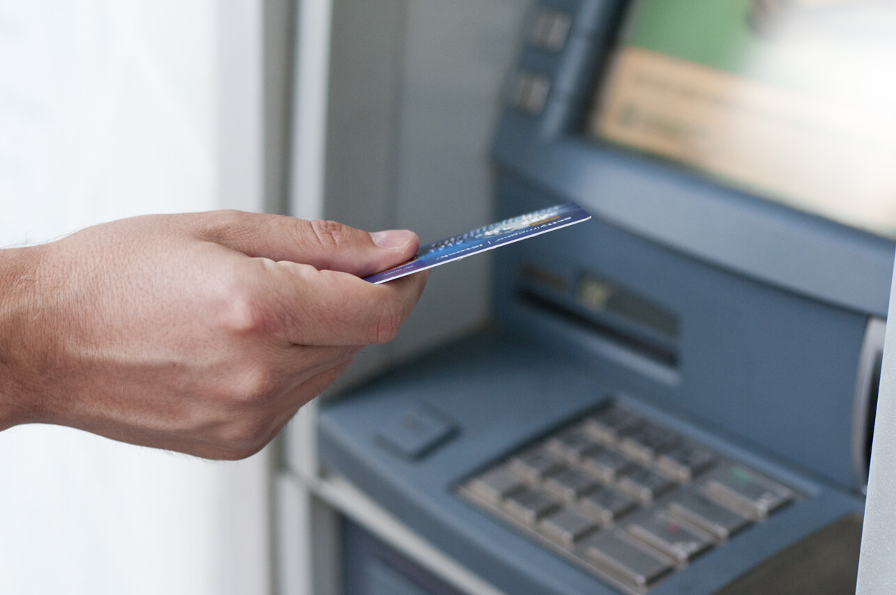 Un hombre sostiene una tarjeta de crédito delante de un cajero